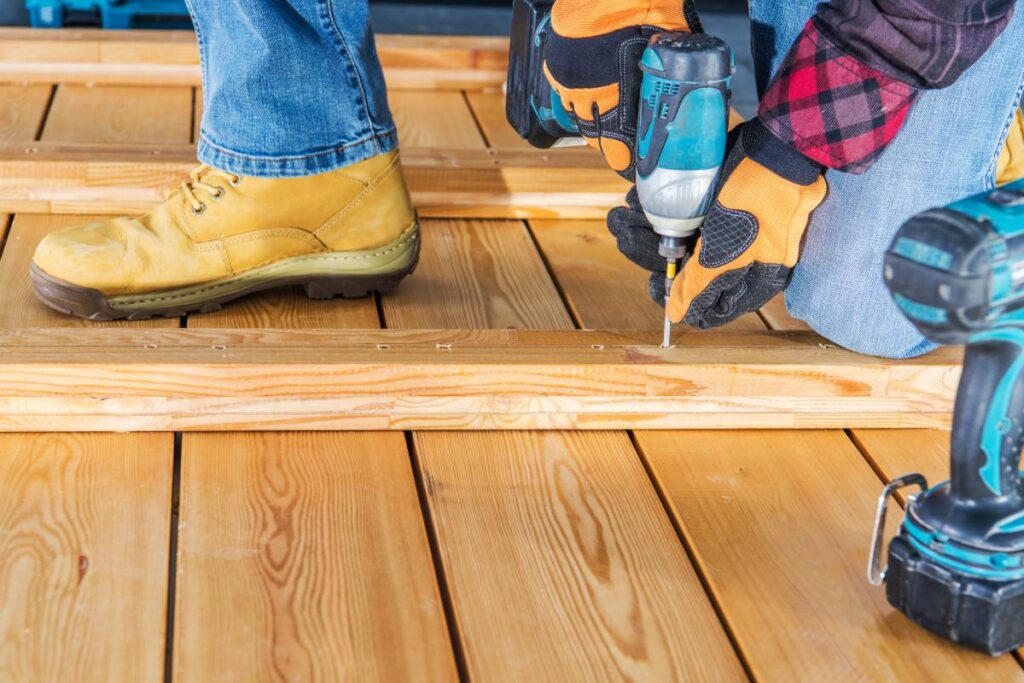 Caucasian Worker Assembling Wood Boards Using Cordless Drill Driver to Build Wooden Wall